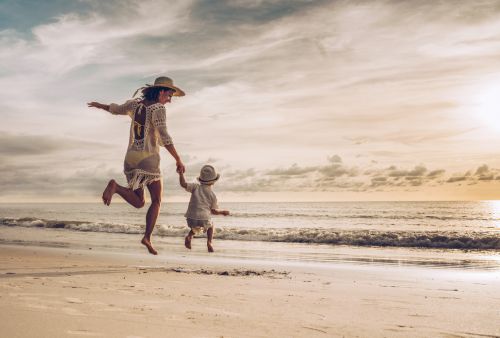 mother and son holding hands while jumping on the beach at sunset. - BartonWood