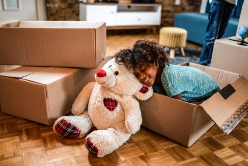Young girl resting in a box next to teddy bear after relocating with after divorce.