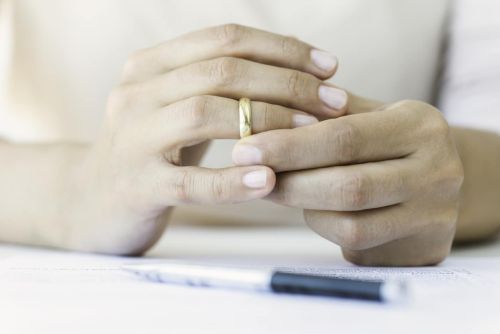 Hands of caucasian female who is about to taking off her wedding ring. Divorce papers are in front of her waiting to be signed. Concept for What Not to Do When Going Through a Divorce.