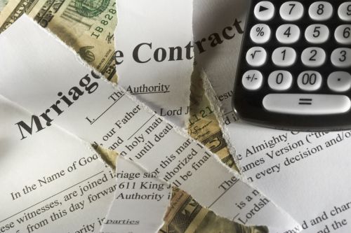 Torn up marriage contract on top of money with a calculator visual concept for legal blog: How Do I Protect Myself Financially in a Divorce?