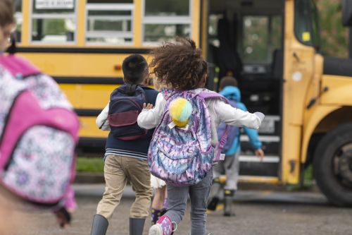 A multi-ethnic group of elementary age children are getting on a school bus happy and eager to get back to school. Visual concept for a family law blog discussing back to school transition tips for co-parents.