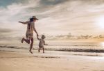 mother and son holding hands while jumping on the beach at sunset. - BartonWood