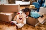 Young girl resting in a box next to teddy bear after relocating with after divorce.