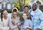 A multi-ethnic blended family of five standing together outdoors in their front yard, smiling and laughing, looking at the camera. The African-American father is in his 40s. Their son and daughter from his prior marriage are 13 year old twins, mixed race African-American and Caucasian. The mother is in her 30s and their youngest son from her prior marriage is 11 years old.