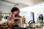 Girl in father's arms helping him cooking his new partner is watching them from the background: concept for How To Introduce Your Child To A New Partner