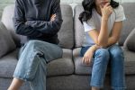 Same sex couple is stressed and not communicating with each other. Sitting on a couch, not touching. Visual concept for a family law blog discussing Utah's same sex divorce laws.